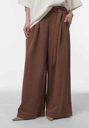 Pantalon marron à jambes larges avec une ceinture assortie en tissu, porté avec des escarpins beiges à bouts pointus et un haut crème ample.
