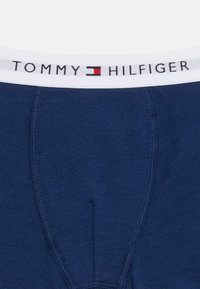 Σκούρο μπλε ανδρικό εσώρουχο με λευκή ζώνη μέσης που φέρει το κείμενο "Tommy Hilfiger" και κόκκινο, λευκό, και μπλε λογότυπο στο κέντρο μπροστά.