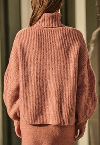 Överdimensionerad rosa tröja med hög ribbad krage och texturerade ballongsärmar. Har kabelstickade detaljer längs ärmarna och en mjuk finish.