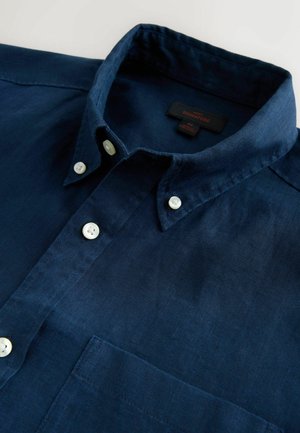 Marineblaues Leinenhemd mit einem Button-Down-Kragen, zwei weißen Knöpfen vorne und einer Brusttasche. Etikett ist innen am Kragen sichtbar.