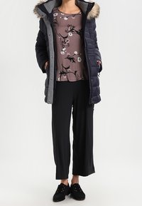 Marinblå puffjacka med pälsdetaljer, gråfoder; blommönstrad mauve-top; svarta vida byxor; svarta snörskor.