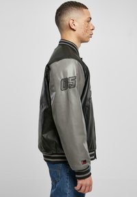 Black leather bomber jacket with grey satin sleeves, featuring ribbed cuffs and collar, an embossed "05" on the left sleeve, and side pockets.