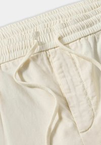Lichte crèmekleurige drawstring broek met een geplooid elastische tailleband, zichtbare stiksels en een gladde katoenstructuur.