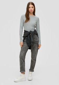 Graues Langarmoberteil kombiniert mit dunkelgrauen Hosen und weißen Plattform-Sneakern. Das Outfit wird durch einen gebundenen schwarzen Sweatshirt an der Taille ergänzt.