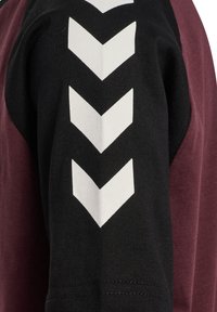 Svart och vinröd T-shirt med design av rundad hals. Har vita chevronmönster på den svarta ärmen, vilket visar kontrasterande färger.