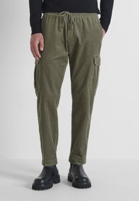 Pantalones cargo de pana en color verde oliva con cinturilla elástica, cordón y bolsillos laterales. Ajustados en los tobillos, con tejido texturizado.