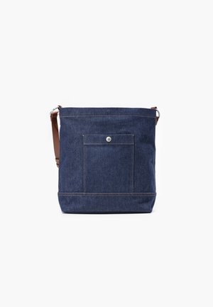 Torba typu tote z ciemnoniebieskiego denimu z przednią kieszenią i zapięciem na guzik, wyposażona w regulowany brązowy pasek na ramię oraz srebrne metalowe okucia.
