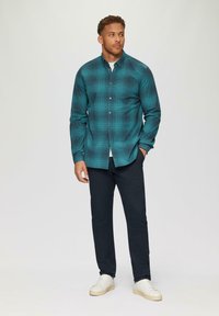 Turquoise en zwarte geruite blouse met knopen, lange mouwen, gecombineerd met donkere broeken en witte sneakers. Strakke stof en gestructureerde pasvorm.