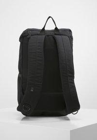Mochila negra con correas de hombro acolchadas, asa superior, cierre de cremallera y tela texturizada. Cuenta con un bolsillo lateral y minimalistas acentos metálicos.