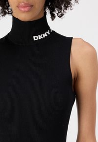 Črni rebrasti brezrokavnik z visokim ovratnikom in belim logotipom "DKNY" na ovratniku, z dodatkom prilegajoče se oblike in mehkega občutka.