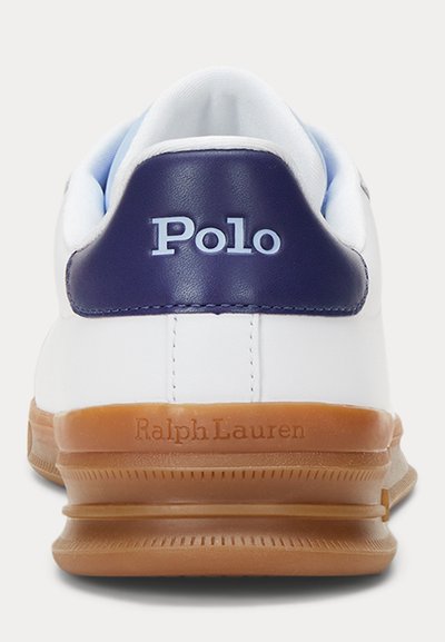 Vit sneaker med en blå läderklack. Har "Polo"-branding och "Ralph Lauren" präglat på gummisulan, med ett texturerat sula-design.