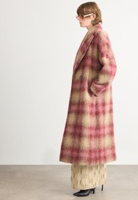 Lang geruit jasje in tinten van roze en geel, gemaakt van een zachte wolmix; heeft een sjawl kraag en zijzakken. Gekleed met een gestructureerde rok.