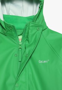 Casaco impermeável verde com gola alta, fecho zíper e forro de fleece macio. Logótipo exibido no peito, textura suave.