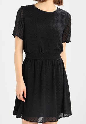 Vestido negro de manga corta con tejido texturizado, cinturilla elástica y falda acampanada. La parte superior presenta un patrón de puntos y escote redondo.