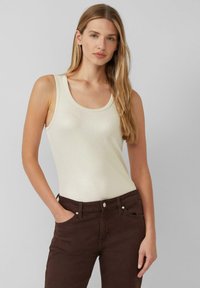 Crème-kleurige, geribbelde tanktop met een ronde hals, gecombineerd met donkerbruine jeans met een knoop en zijzakken. Gladde textuur.