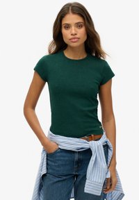 Grøn kortærmet T-shirt lavet af blødt stof, med rund halsudskæring og et lille logo på kanten, parret med blå jeans og en stribet skjorte knyttet om taljen.
