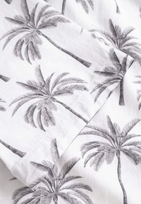 Tessuto in cotone con una stampa di palme in bianco e nero. Il design presenta fronde e tronchi dettagliati su uno sfondo chiaro.