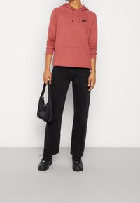 Röd hoodie med framficka och svart Nike-logotyp, matchad med svarta raka jeans och svarta sneakers. Bär en svart handväska.