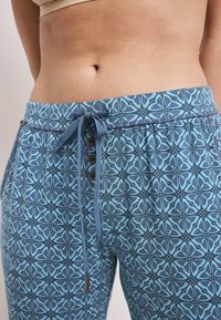 Blauwe patroonbroek met een trekkoord in de taille, voorzien van knoopdetails en een geometrisch ontwerp in licht- en donkerblauwe tinten.