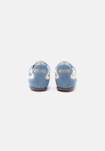 Chaussures en denim bleu clair à enfiler, avec des accents blancs effilochés et "MOSCHINO" brodé en doré sur les languettes du talon, vues de dos.