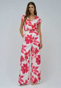 Salopette floreale a maniche corte, con una trama nei toni del rosa e del bianco, design con bottoni sul davanti, vestibilità ampia e tessuto morbido e leggero.