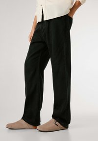 Svarta denimbyxor med avslappnad passform, med minimal sömnad och sidofickor. Kombineras med beige mocka slip-on skor med spänne.