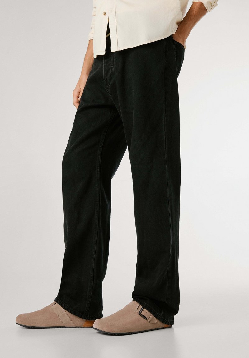 Svarta denimbyxor med avslappnad passform, med minimal sömnad och sidofickor. Kombineras med beige mocka slip-on skor med spänne.