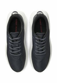 Marineblaue Sportschuhe mit strukturiertem Obermaterial, abgerundeter weißer Sohle und grauen Schnürsenkeln. Verfügen über eine Zuglasche an der Ferse für leichtes An- und Ausziehen.