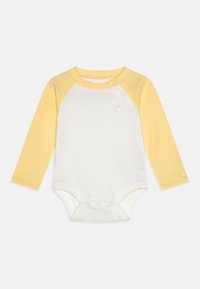 Langermet bodystocking med hvit kropp og gule raglan-ermer, laget av myk bomull med trykknapper på bena for enkel skifting.