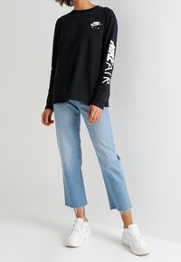Svart långärmad T-shirt med vitt Nike-logotyp och texten "AIR". Kombineras med ljusblå cropped jeans och vita sneakers. Slen bomullstextur.