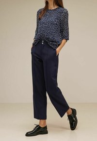 Navy Bluse mit geometrischem Muster, kombiniert mit maßgeschneiderten navyblauen Hosen und schwarzen Schnürschuhen. Weicher Stoff und lockere Passform.