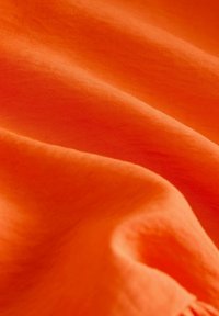 Levande orange tyg med en slät textur, som har mjuka draperingar och subtila nyansvariationer, vilket skapar ett visuellt rikt utseende.