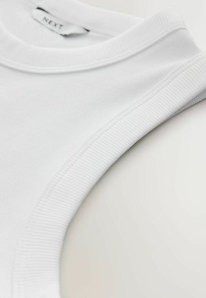 Valge puuvillane topp, millel on sooniline kaelus ja sile pind. Krae sees on nähtav silt "NEXT".