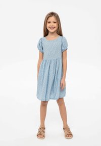 Helles blaues Blumenkleid mit kurzen Puffärmeln, rundem Halsausschnitt und gerafftem Rock. Kombiniert mit beigefarbenen Sandalen.