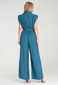 Morska kombinacja z szerokimi nogawkami, krótkimi rękawami, elastycznym paskiem i kołnierzykiem. Gładki materiał z dopasowanym górnym częścią i luźnym krojem.