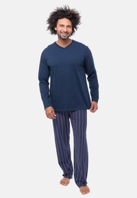 Maglietta a maniche lunghe blu marino con scollo a V e tasca, abbinata a pantaloni da pigiama a righe blu, rossi e bianchi. Tessuto di cotone morbido, vestibilità comoda.