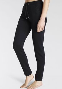 Schwarze Jogginghose aus weichem, dehnbarem Material. Mit einem Kordelzugbund, schmal zulaufenden Beinen und Seitennähten. Minimalistisches Design.