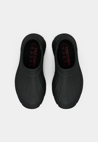 Tamancos de borracha pretos com uma textura de superfície estriada, apresentando uma palmilha almofadada com "Tretorn Kassl" impresso em bordô.