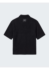 Chemise noire à manches courtes texturée avec col, vue de dos, avec un petit écusson carré sous le col.