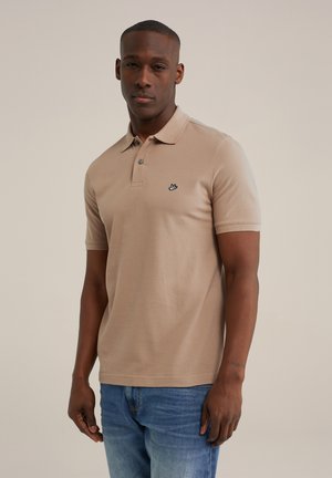 Beige Poloshirt aus weichem Material mit Kragen, kurzen Ärmeln und einem gestickten Logo auf der linken Brust. Kombinierbar mit blauen Jeans.