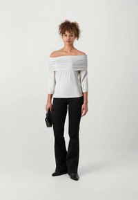 Off-shoulder hvit topp med trekvartlange ermer, kombinert med svarte vide bukser. Plagget har en jevn tekstur og enkelt design.