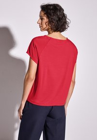 Top rouge à manches courtes avec une coupe décontractée, un col rond et des détails de couture visibles. Associe à un pantalon large bleu marine.