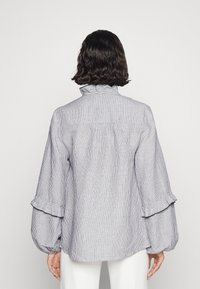 Chemise à manches longues à rayures avec un col montant, un détail froncé et des poignets à volants. Confectionnée en tissu léger bleu et blanc.