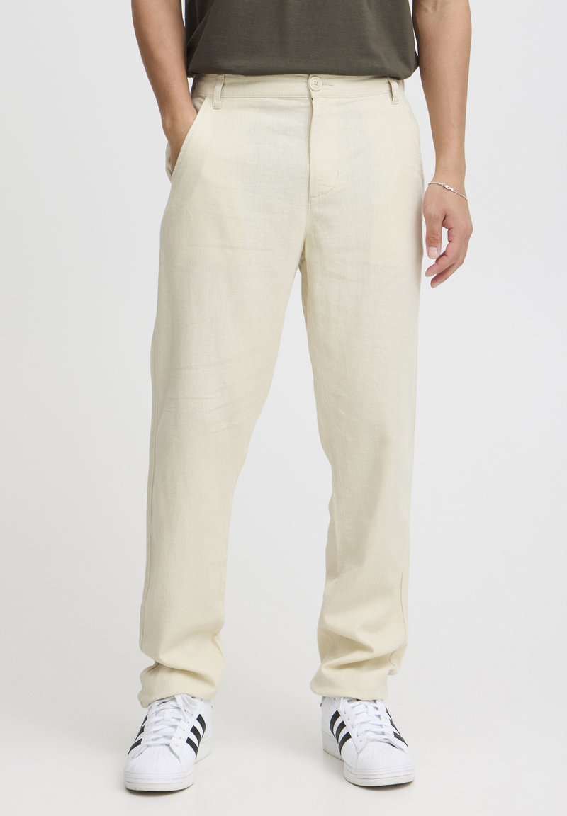 Linnenbukser i lys beige med en afslappet pasform, med sidelommer og knaplukning, parret med hvide sneakers.