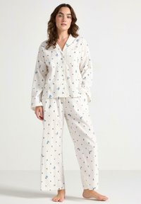 Witte bloemenpyjama set met een knoopjesblouse met lange mouwen en bijpassende wijde broek, versierd met blauwe en groene bloemmotieven.