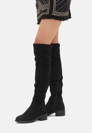 Black over-the-knee boots made of soft suede, featuring a flat heel, zip closure on the side, and a fitted design enhancing leg shape.