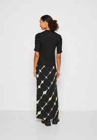 Black top with gathered sleeves, paired with a long patterned skirt featuring a white abstract diamond design and chunky black footwear.