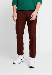 Burgundské kostičkované kalhoty s úzkým střihem, které mají kostkovaný vzor a boční kapsy, doplněné bílými sportovními botami.