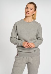 Szary sweatshirt z okrągłym dekoltem, ściągaczami przy mankietach i u dołu, wykonany z miękkiego materiału. Posiada subtelny akcent z logo na pasku.