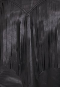 Top de cuero negro con detalles de flecos verticales, escote en forma de V y textura suave. El diseño enfatiza una apariencia de varias capas.